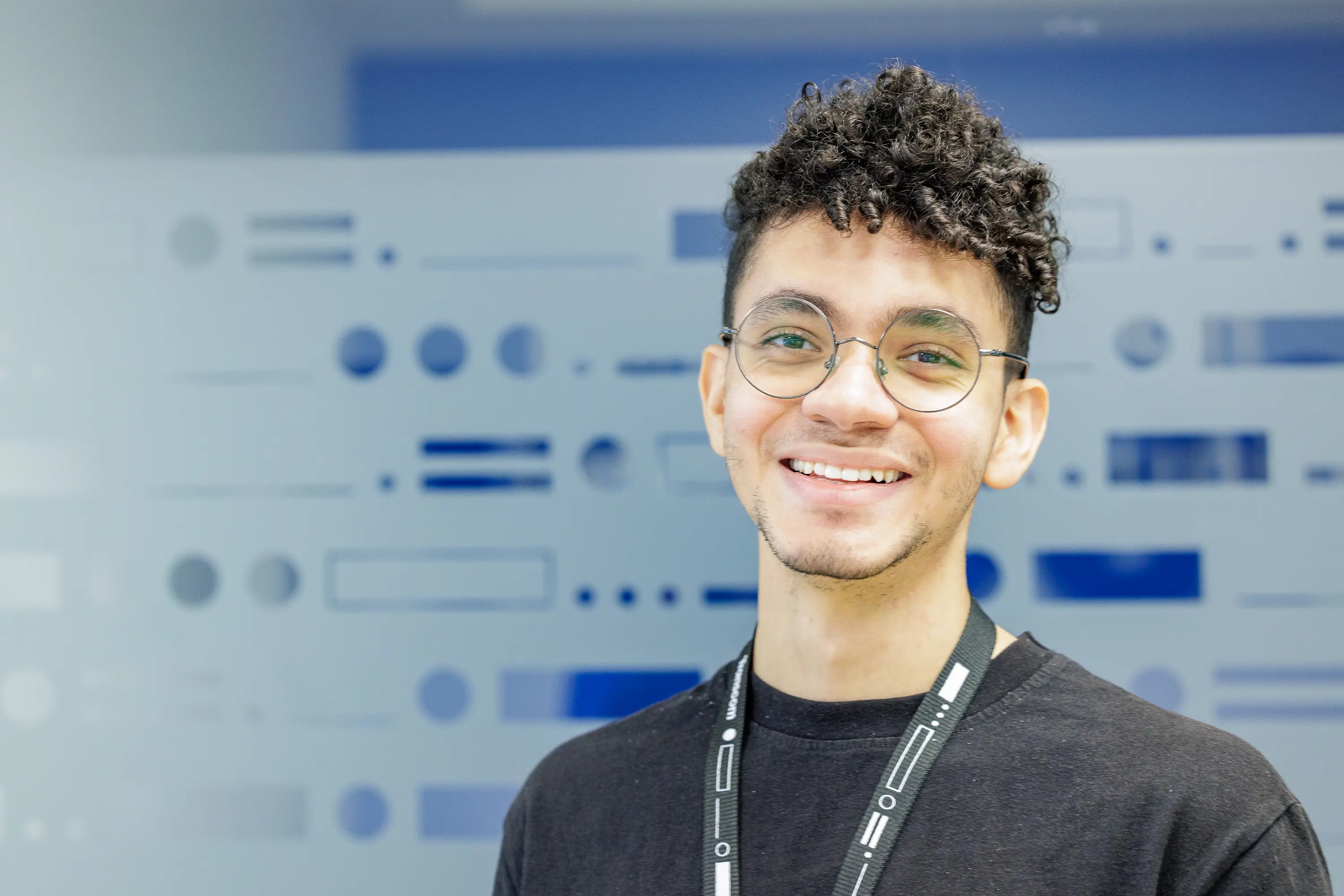 Smiling young man wearing glasses with a tech-themed blurred background