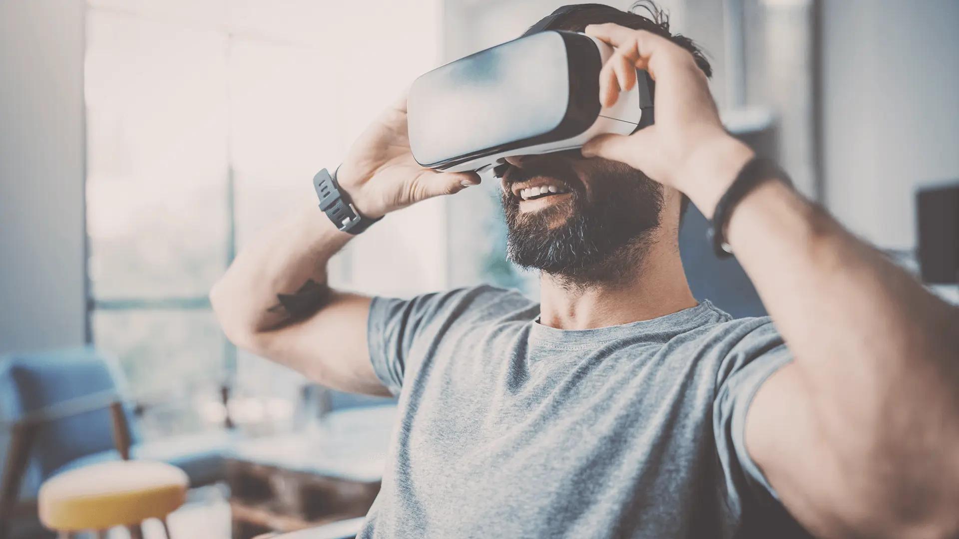 A bearded man wearing a virtual reality headset, smiling and enjoying an immersive VR experience in a modern indoor setting.