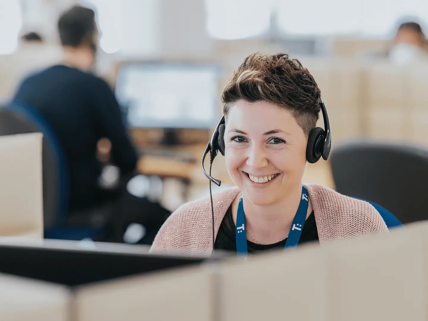 A smiling customer service agent wearing a headset in a busy office