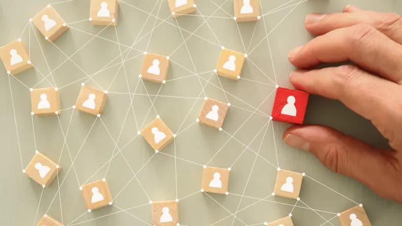 A hand placing a red block with a user icon among interconnected wooden blocks representing a social or business network