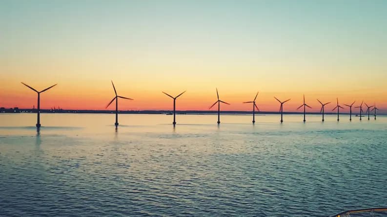 A row of offshore wind turbines at sunset over calm waters
