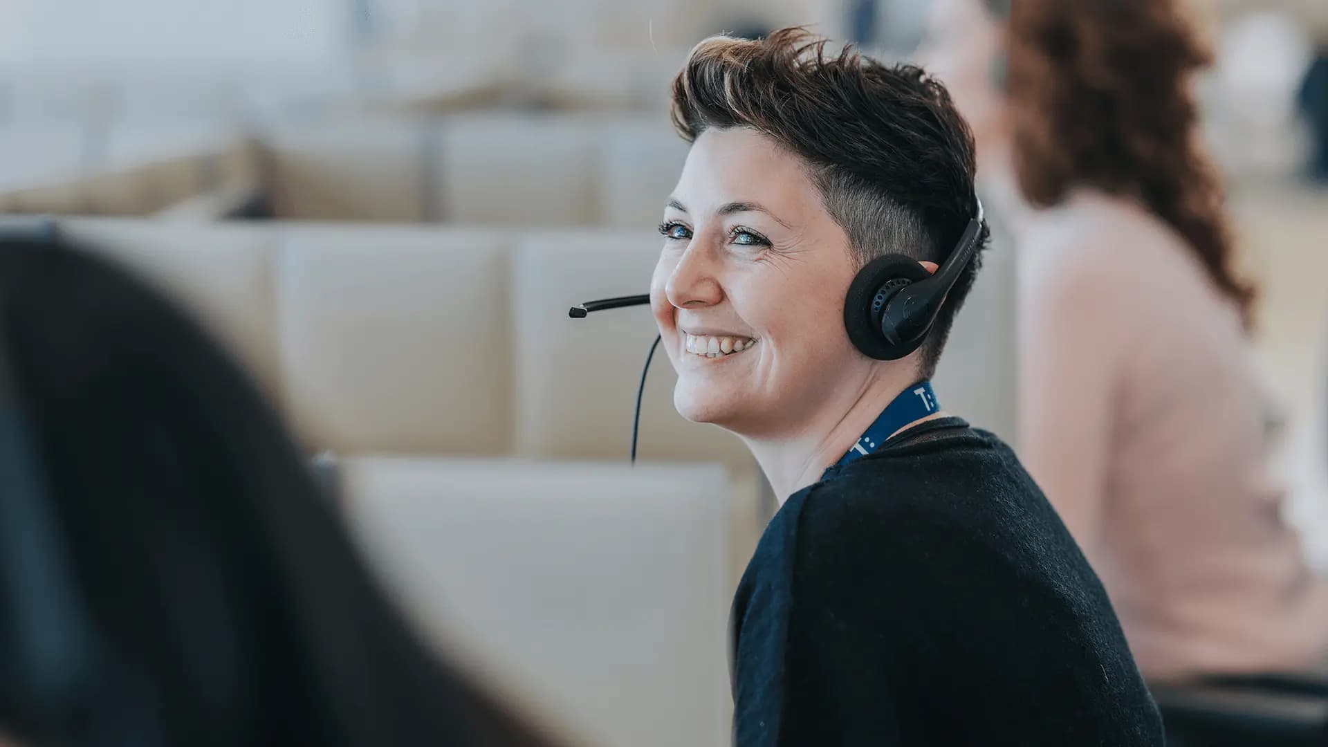 A smiling customer support agent wearing a headset in an office environment.